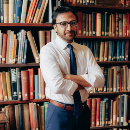 Nikhil Goyal standing in front of a wall of books